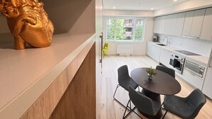 Een moderne keuken met witte kasten, een eethoek met een ronde tafel en stoelen, en een groot gouden sculptuur op het aanrecht.