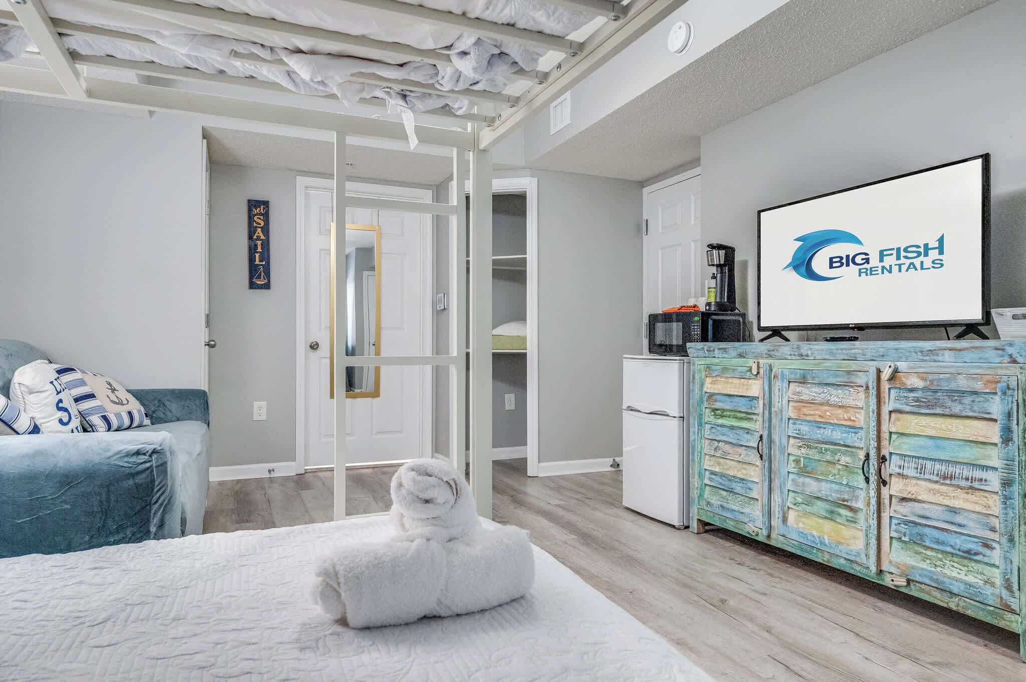 A hotel room with a bed, a white towel, a television, and a kitchenette.