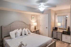 A bedroom with a bed, bedside tables, a lamp, a door, and a window with blinds. - Studio, Barefoot Yacht Club, Saltwater Pools, New! (North Myrtle Beach)