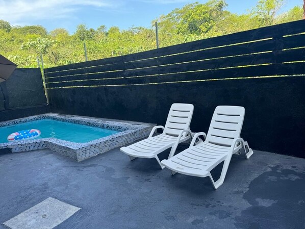 Una piscina con dos sillas reclinables blancas y un flotador inflable pequeño.