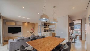 Una sala de estar moderna con una mesa de comedor de madera, un sofá gris y un televisor de pantalla plana montado en la pared.