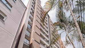Un edificio residencial de gran altura con balcones, un cartel que dice “SAN JOSE apartamentos” y un jardín bien cuidado.