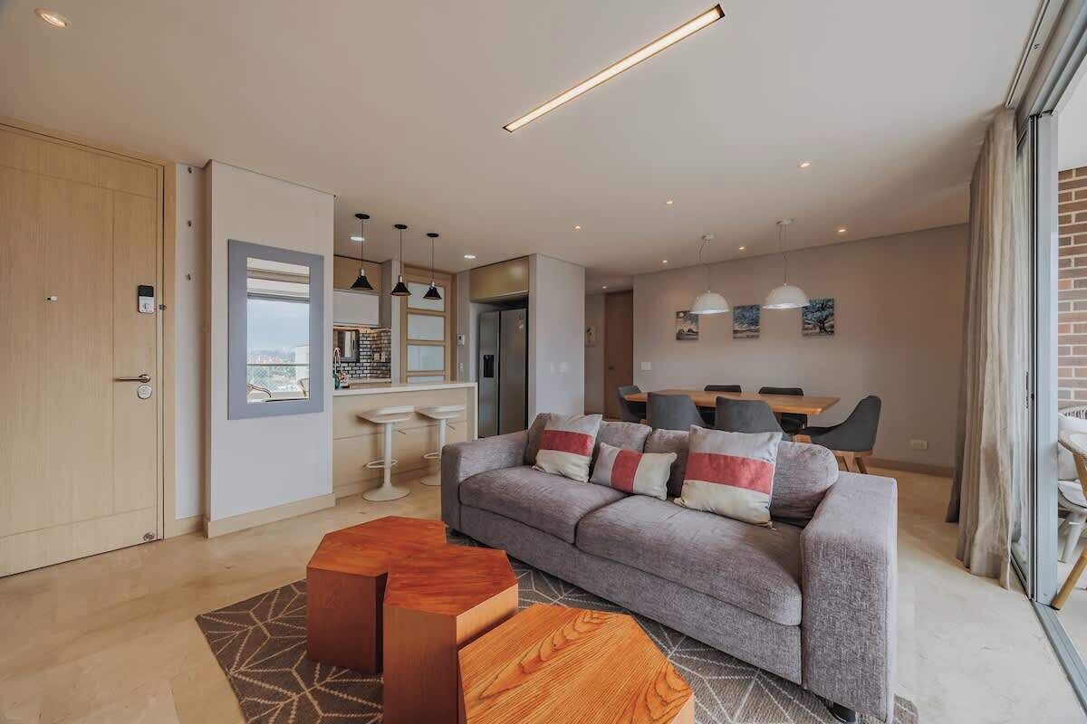 A modern living room with a grey sofa, wooden coffee table, and a dining area with a table and chairs.