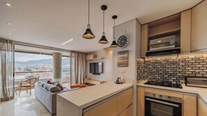 Una cocina moderna con una isla central, horno integrado y microondas. Hay un ventanal con vistas a la ciudad.