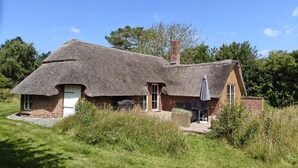Una casa de techo de paja con paredes de ladrillo, una chimenea y un pequeño patio con muebles de exterior.