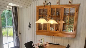 Un comedor con mesa de madera, sillas negras, individuales tejidos y un mueble con puertas de vidrio en la parte superior.