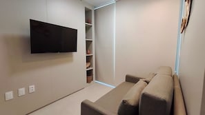 A modern living room with a flat-screen TV mounted on the wall, a built-in seating area, and a shelving unit with decorative items. - Itah Residence - Condomínio Beira-Mar (Ipojuca)