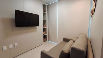 Uma sala de estar moderna com televisão de tela plana na parede, um espaço de estar integrado e uma estante com objetos decorativos.