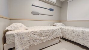 Quarto pequeno com duas camas, um remo fixado na parede e uma janela.