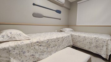 Quarto com duas camas, um banco, remo fixado na parede e ar-condicionado.