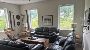 A living room with a black leather sofa set, a wooden coffee table, and a wooden chair. There are two windows providing natural light, and a framed picture on the wall. - 3Bed3.5Bath @ Burk’s Falls's View (Burk's Falls)