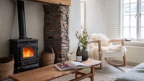 Una sala de estar acogedora con una chimenea de piedra, una mesa de madera con un libro, una silla y un jarrón con flores.