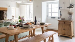 Una mesa de comedor de madera dispuesta con comida y vino, un banco y un aparador rústico.