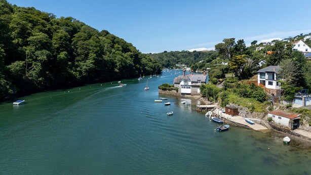 Un río con barcos, rodeado de casas y vegetación.