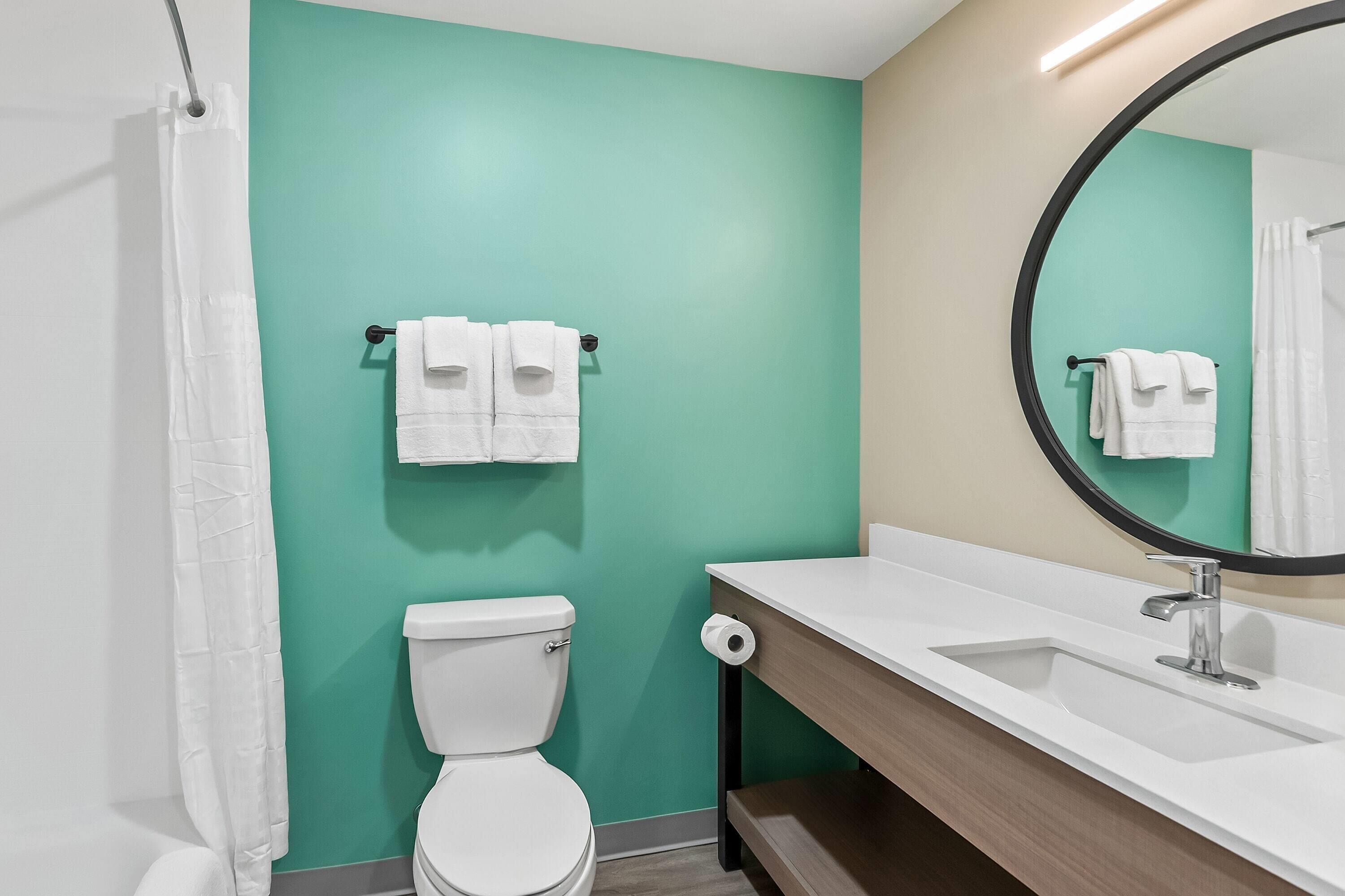 A bathroom with a white toilet, a sink with a mirror, and a towel rack with two white towels.