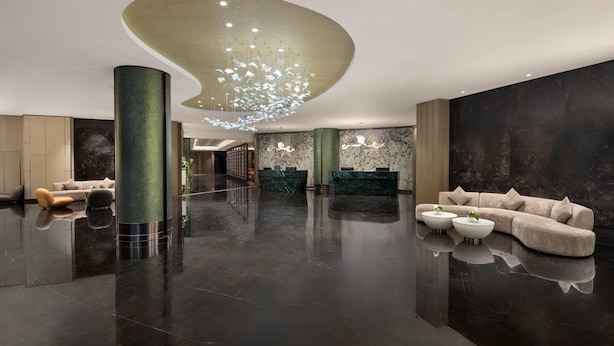 Een ruime lobby met een moderne kroonluchter, een receptiebalie en een zithoek met banken en salontafels.