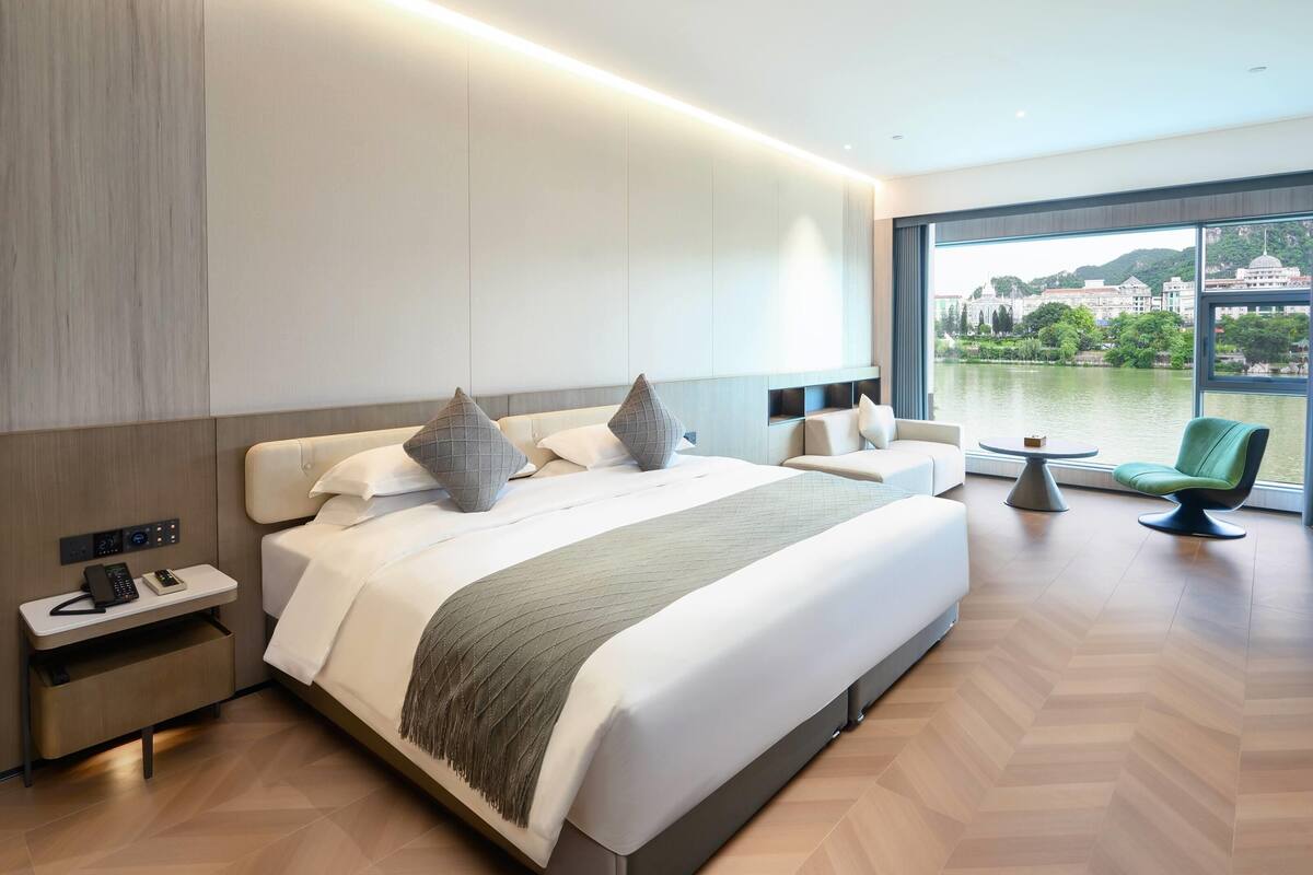 A modern hotel room with a large bed, bedside tables, a small table, and a chair.