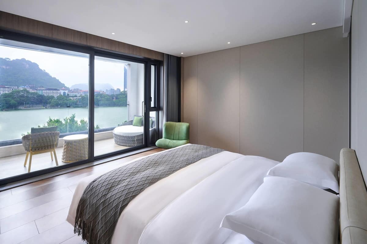 A modern bedroom with a large bed, a view of a river, and a balcony with seating.