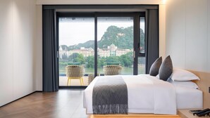 A modern hotel room with a large bed, a view of a cityscape and mountains, and a balcony with chairs. - Wyndham Garden Liuzhou Wuxing Street (Liuzhou)