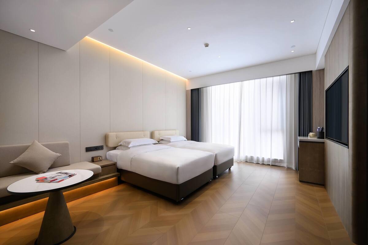 A modern hotel room with a large bed, a sofa, a small table, and a TV.