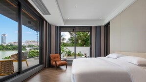 A modern hotel room with a large bed, a chair, a small table, and a view of a cityscape and water. - Wyndham Garden Liuzhou Wuxing Street (Liuzhou)