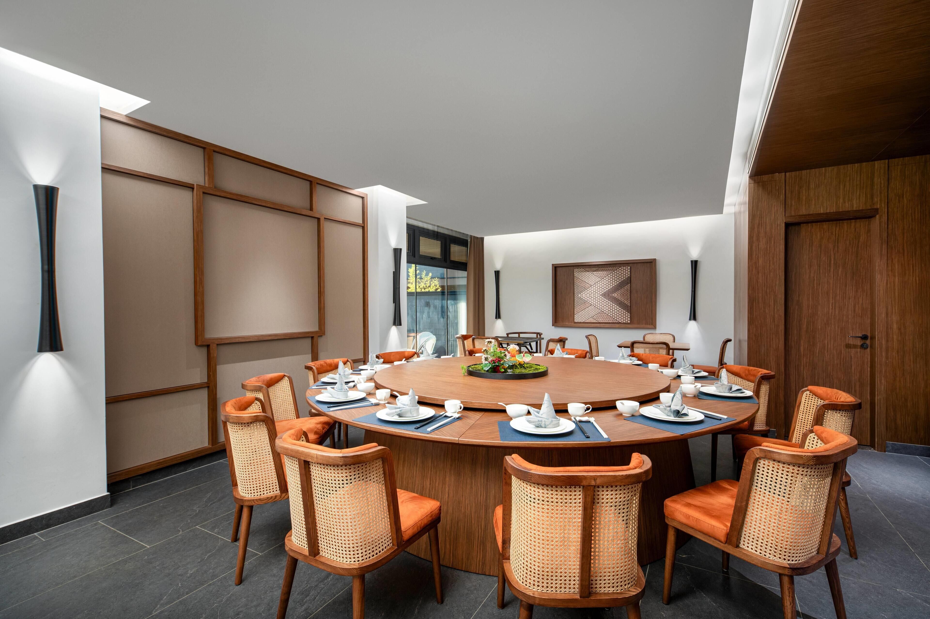 Une salle de réunion moderne avec une table ronde, des chaises orange et un mur de séparation en bois.