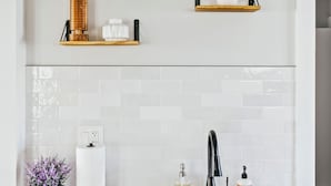 A modern kitchen with white cabinetry, a stainless steel sink, and two wooden shelves with decorative items. - Charming 2-bedroom condo in marvelous Chicago (Chicago)
