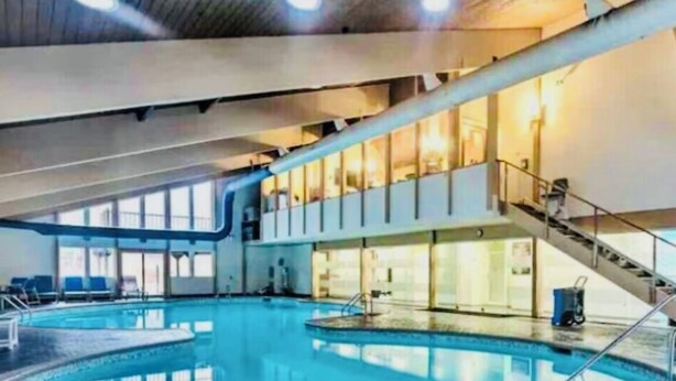 Una piscina interna con una vista chiara dell'area della piscina, una scala che conduce a un livello superiore e un’area salotto con sedie.