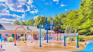 Un'area giochi all'aperto con diversi giochi, tra cui altalene e strutture per arrampicarsi, circondata da alberi e un edificio sullo sfondo.