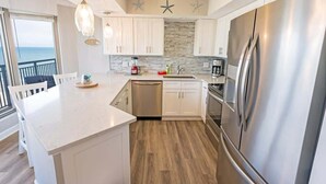 A modern kitchen with white cabinets, a stainless steel refrigerator, and a view of the ocean. - New 16th Floor Luxury,Breathtaking Views,Brighton! (Myrtle Beach)