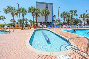 A swimming pool with lounge chairs, palm trees, and a building in the background. - Caravelle 1044 (Myrtle Beach)