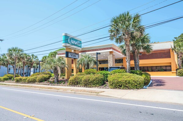 A hotel with a prominent sign, palm trees, and a clear sky.
