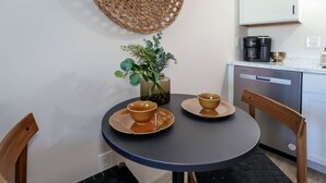Ein kleiner runder Tisch mit zwei passenden Schüsseln und Untertassen, eine Vase mit Grünpflanzen und eine Kaffeemaschine auf der Arbeitsfläche.