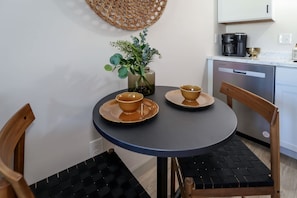 A small round table with two matching bowls and saucers, a vase with green foliage, and a coffee maker on the counter.