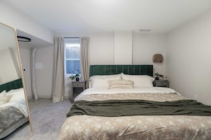 Un dormitorio con una cama, una mesita de noche, un espejo, una ventana con cortinas y un ventilador de pared.