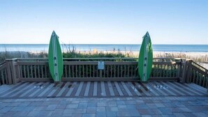 A wooden deck with two green surfboards leaning against a railing, overlooking a beach.