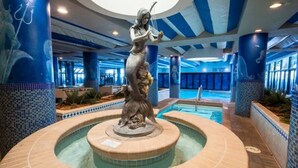 A pool area with a statue in the center, surrounded by blue-tiled walls and columns.