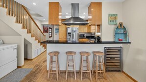 Une cuisine moderne dotée d’un îlot central, de tabourets de bar en bois, d’une hotte de cuisine en acier inoxydable et d’un escalier avec des rampes en bois.