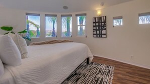 A bedroom with a large bed, multiple windows, a wall-mounted light, and a patterned rug. - Villa Beryl - Lux 4BR/3BA - Rooftop Deck (San Diego)