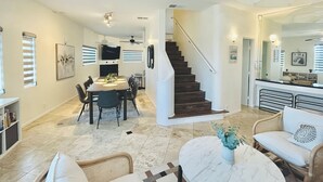 A spacious living area with a dining table, sofas, a staircase, and a kitchen area. - Villa Beryl - Lux 4BR/3BA - Rooftop Deck (San Diego)