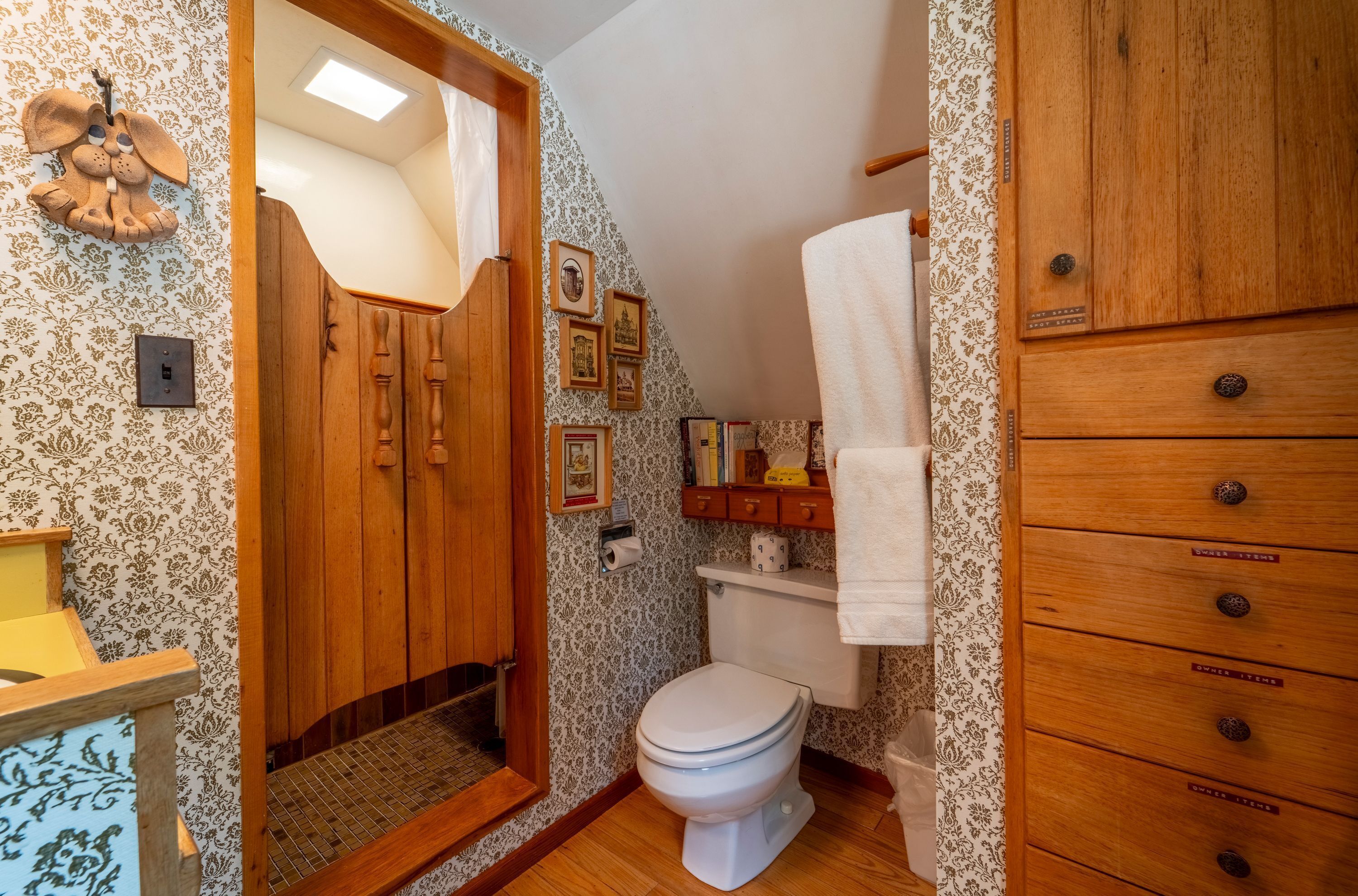 A bathroom with a wooden door, a toilet, a shelf with toiletries, and a towel rack.