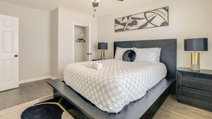 Ein Schlafzimmer mit Bett, Nachttischen, Deckenventilator, Wandbild und Kleiderschrank mit Kleidung.