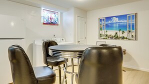 A dining area with a round table and four black chairs, a white door, a stained glass window, and a beach scene painting on the wall. - 5 Mi to Trilith Studios: Apt w/ Furnished Pergola (Fayetteville)