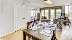 A dining area with a wooden table set for four, a sofa, and a TV in the background. - Swim, Fish & Suntan: Cozy Corpus Christi Retreat (Corpus Christi)