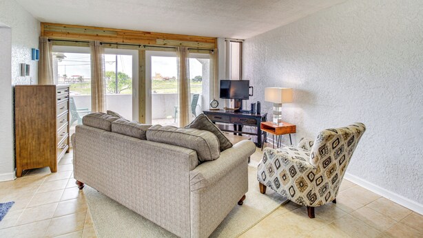 A living room with a sofa, armchair, TV, and desk. - Swim, Fish & Suntan: Cozy Corpus Christi Retreat (Corpus Christi)