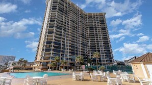 A high-rise hotel with multiple balconies, a swimming pool, and outdoor seating areas.