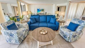 A modern living room with a blue sofa, two patterned armchairs, a wooden coffee table, and a television in the background.
