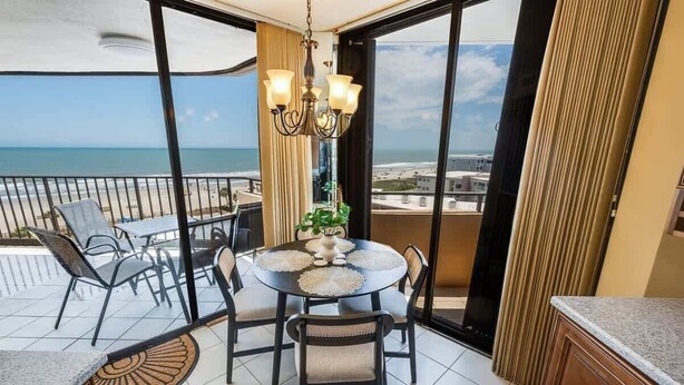 A balcony with a table and chairs, a chandelier, and a view of the beach.
