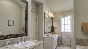 Un baño con un espejo grande, dos lavamanos, un perchero para toallas y una ventana.