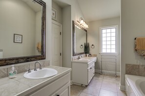 Un bagno con un ampio specchio, due lavandini, un portascopino e una finestra.